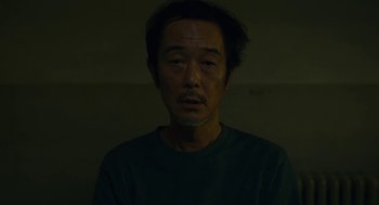 Movie still from “Shoplifters” (2018), directed by Kore-eda Hirokazu – A man in a green shirt is looking at the camera; Medium shot, Low angle