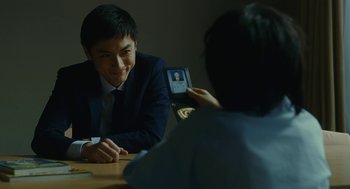 Movie still from “Shoplifters” (2018), directed by Kore-eda Hirokazu – A man sitting in front of a woman holding up a cell phone; Close Up shot, Over the shoulder angle