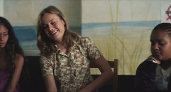 Movie still from “Short Term 12” (2013), directed by Destin Daniel Cretton – A woman sitting at a table smiling for the camera; Medium shot, Over the shoulder angle