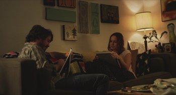 Movie still from “Short Term 12” (2013), directed by Destin Daniel Cretton – A man and a woman sitting on a couch looking at books; Medium shot, Over the shoulder angle