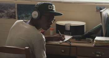 Movie still from “Short Term 12” (2013), directed by Destin Daniel Cretton – A man wearing headphones writing on a piece of paper; Medium shot, Over the shoulder angle