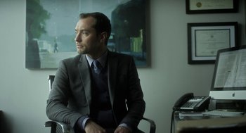 Movie still from “Side Effects” (2013), directed by Steven Soderbergh – A man in a suit sitting in front of a window; Medium shot, Low angle
