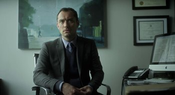 Movie still from “Side Effects” (2013), directed by Steven Soderbergh – A man in a suit and tie sitting in front of a painting; Medium shot, Low angle