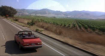 Movie still from “Sideways” (2004), directed by Alexander Payne – A red car driving down a road near a field; Extreme Wide shot, High angle
