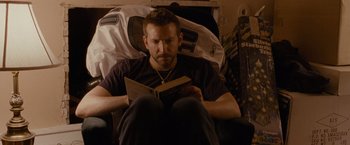 Movie still from “Silver Linings Playbook” (2012), directed by David O. Russell – A man sitting in a chair while reading a book; Medium shot, High angle