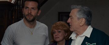 Movie still from “Silver Linings Playbook” (2012), directed by David O. Russell – Two men and a woman standing next to each other in a room; Medium shot, Over the shoulder angle
