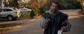 Movie still from “Silver Linings Playbook” (2012), directed by David O. Russell – A man is walking down the street holding something in his hand; Medium shot, Over the shoulder angle