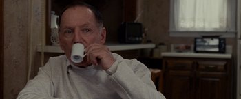 Movie still from “Silver Linings Playbook” (2012), directed by David O. Russell – An older man is drinking from a white cup; Medium shot, Low angle