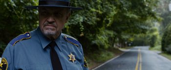 Movie still from “Sinister” (2012), directed by Scott Derrickson – A man in a police uniform standing on the side of the road; Close Up shot, Over the shoulder angle