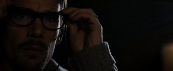 Movie still from “Sinister” (2012), directed by Scott Derrickson – A person wearing glasses and a sweater; Close Up shot, Low angle