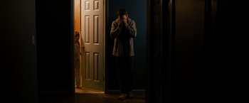 Movie still from “Sinister” (2012), directed by Scott Derrickson – A woman standing in a doorway holding her hands up to her face; Wide shot, Over the shoulder angle