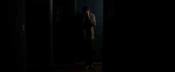 Movie still from “Sinister” (2012), directed by Scott Derrickson – A man standing in a dark room holding his hands to his face; Medium shot, Low angle
