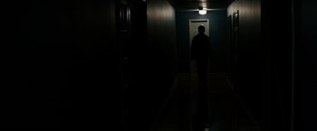 Movie still from “Sinister” (2012), directed by Scott Derrickson – A person walking in a dark hallway with a door open; Wide shot, Low angle