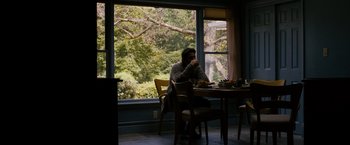 Movie still from “Sinister” (2012), directed by Scott Derrickson – A man sitting at a table drinking a cup of coffee; Wide shot, Over the shoulder angle