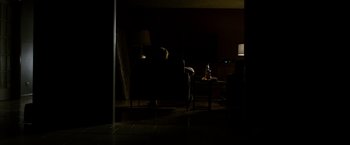 Movie still from “Sinister” (2012), directed by Scott Derrickson – A person sitting on a couch in a dark room; Wide shot, Over the shoulder angle