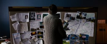Movie still from “Sinister” (2012), directed by Scott Derrickson – A man standing in front of a wall covered in photos; Medium shot, High angle