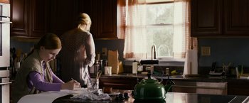 Movie still from “Sinister” (2012), directed by Scott Derrickson – A woman standing in a kitchen next to a sink; Medium shot, Over the shoulder angle