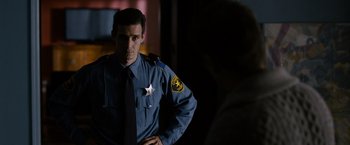 Movie still from “Sinister” (2012), directed by Scott Derrickson – A man in a police uniform standing next to a woman; Medium shot, Over the shoulder angle