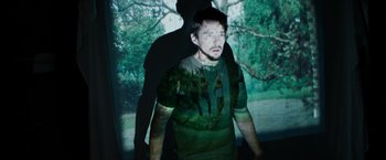 Movie still from “Sinister” (2012), directed by Scott Derrickson – A man standing in front of a window wearing a t - shirt; Medium shot, Low angle