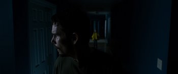 Movie still from “Sinister” (2012), directed by Scott Derrickson – A man standing in a dark room with his head turned to the side; Medium shot, Over the shoulder angle