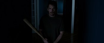 Movie still from “Sinister” (2012), directed by Scott Derrickson – A man holding a baseball bat while standing in a dark room; Medium shot, High angle