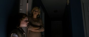 Movie still from “Sinister” (2012), directed by Scott Derrickson – A woman standing next to a door in a dark room; Medium shot, Over the shoulder angle