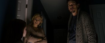 Movie still from “Sinister” (2012), directed by Scott Derrickson – A man and a woman standing next to each other in a dark room; Medium shot, Low angle