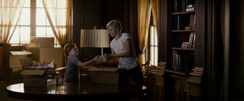 Movie still from “Sinister” (2012), directed by Scott Derrickson – A woman and a child are handing a box; Medium shot, Over the shoulder angle