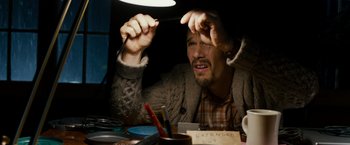 Movie still from “Sinister” (2012), directed by Scott Derrickson – A man sitting in front of a table holding a pen; Close Up shot, High angle