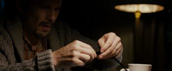 Movie still from “Sinister” (2012), directed by Scott Derrickson – A man is knitting a sweater with a needle and thread; Close Up shot, High angle