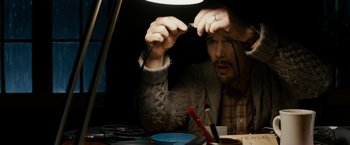 Movie still from “Sinister” (2012), directed by Scott Derrickson – A man sitting at a table holding a pair of scissors; Close Up shot, High angle