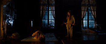 Movie still from “Sinister” (2012), directed by Scott Derrickson – A woman standing in a dark room next to a man laying on the ground; Wide shot, High angle