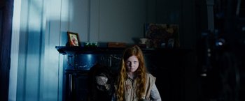 Movie still from “Sinister” (2012), directed by Scott Derrickson – A young girl standing in front of a fireplace; Medium shot, Over the shoulder angle