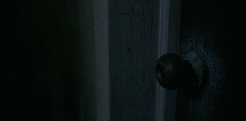 Movie still from “Smile” (2022), directed by Parker Finn – A door handle in a dark room with peeling paint on the wall; Extreme Close Up shot, High angle