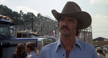 Movie still from “Smokey and the Bandit” (1977), directed by Hal Needham – A man in a cowboy hat standing in front of a roller coaster; Close Up shot, Low angle