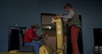 Movie still from “Smokey and the Bandit” (1977), directed by Hal Needham – Two men are working on a machine in a warehouse; Medium shot, Low angle