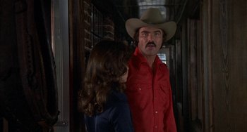 Movie still from “Smokey and the Bandit” (1977), directed by Hal Needham – A man in a cowboy hat talking to a woman in a red shirt; Medium shot, Over the shoulder angle