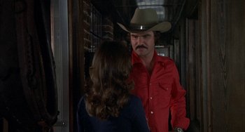 Movie still from “Smokey and the Bandit” (1977), directed by Hal Needham – A man in a cowboy hat talking to a woman in a red shirt; Medium shot, Over the shoulder angle