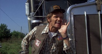 Movie still from “Smokey and the Bandit” (1977), directed by Hal Needham – A man in a cat hat and a brown vest standing in front of a truck; Close Up shot, Low angle