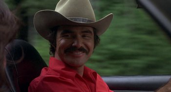 Movie still from “Smokey and the Bandit” (1977), directed by Hal Needham – A man in a red shirt and a cowboy hat; Close Up shot, Over the shoulder angle