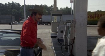Movie still from “Smokey and the Bandit” (1977), directed by Hal Needham – A man wearing a cowboy hat at a gas station; Medium shot, Over the shoulder angle
