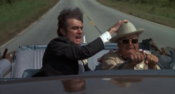 Movie still from “Smokey and the Bandit” (1977), directed by Hal Needham – A man in a suit and a hat in the back of a car; Close Up shot, Over the shoulder angle