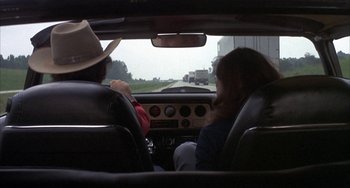Movie still from “Smokey and the Bandit” (1977), directed by Hal Needham – A man and a woman riding in the back of a car; Wide shot, Over the shoulder angle