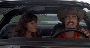 Movie still from “Smokey and the Bandit” (1977), directed by Hal Needham – A man and a woman sitting in the drivers seat of a car; Close Up shot, Over the shoulder angle