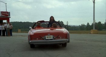Movie still from “Smokey and the Bandit” (1977), directed by Hal Needham – A woman sitting in the back seat of a red car; Wide shot, High angle
