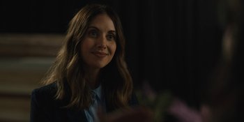 Movie still from “Somebody I Used to Know” (2023), directed by Dave Franco – A woman with long brown hair sitting in front of flowers; Close Up shot, Over the shoulder angle