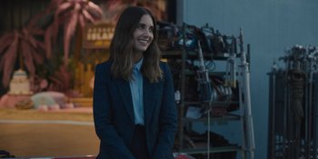 Movie still from “Somebody I Used to Know” (2023), directed by Dave Franco – A woman wearing a suit and smiling for the camera; Medium shot, Over the shoulder angle