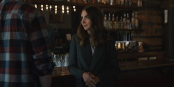 Movie still from “Somebody I Used to Know” (2023), directed by Dave Franco – A woman standing in front of a bar in a suit; Medium shot, Over the shoulder angle