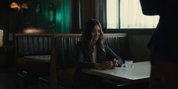 Movie still from “Somebody I Used to Know” (2023), directed by Dave Franco – A woman sitting at a table in front of a glass of water; Medium shot, Over the shoulder angle