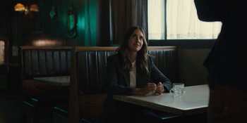 Movie still from “Somebody I Used to Know” (2023), directed by Dave Franco – A woman sitting at a table in front of a glass of water; Medium shot, Over the shoulder angle